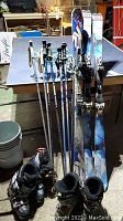 Photo showing all the ski equipment on a ping pong table including three pairs of ski poles, two pairs of skis, and two pairs of ski boots in black and blue colors with visible scuffs.