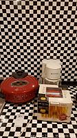 Red West Bend rotary snack oven, white Proctor-Silex coffee maker, and boxed Atlas 150 pasta maker on countertop with checkered tile background.
