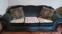 Front view of green three seat sofa with three floral seat cushions and two floral throw pillows.