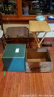 Overview of four items on hardwood floor: storage ottoman, milk crate, wicker table, folding tray stand