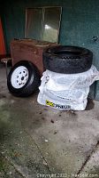 Lot showing four M+S tires sized LT245/75R16 stacked on a wrapped pallet, one tire mounted on a white rim leaning against the pallet. Old cabinet and mirrors in background.