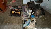 Photo shows a DeWalt tool bag, a black pouch with hand tools, a rusty tool belt, and painting supplies in a white paint tray including roller and brush, plus a plastic bin with various tools and hardware.