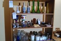 Wide view of wooden shelves holding assorted items including vases, bottles, cups, figurines and glassware