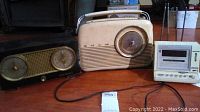 Three vintage radios including a black RCA Victor radio with dual dials, white portable radio, and small clock radio shown together.
