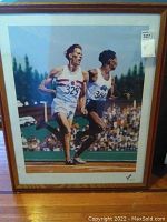 Framed poster of two runners on a race track, with crowd and trees background.