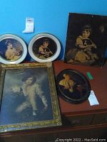 Five framed art prints featuring children and a dog, arranged on a brown desk against a blue wall.
