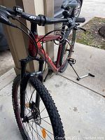 Mountain bike angled from front showing frame, front suspension, front tire, handlebars with gear shifters and brake levers, front light and front disc brake.