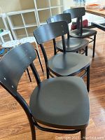 Four black wood laminate dining chairs lined up on wood floor, view from the front and side showing seats and backs.