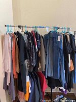 Full view of the metal two-tier clothes rack on wheels loaded with assorted clothes on plastic and wire hangers.