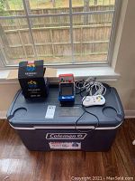 Photo showing the Coleman cooler with Neo Geo Mini game system, controller, and box placed on top near a window