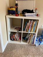 Front view of white laminate storage shelf with 4 cube compartments showing some books inside compartments.