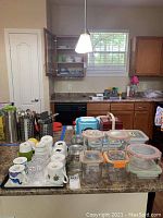 Overall kitchen countertop view showing assorted cups placed on a tray, and multiple Glasslock storage containers with lids arranged next to the tray.