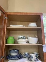 Kitchen cabinet shelf with assorted dishes including green bowls, white serving pitcher, small plates with floral patterns