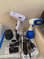 Photo showing Conair hair dryer, handheld steamer, clippers with attachments, and Thermacell device on a small white shelf.