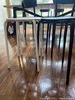 Photo showing four stools with metal legs under a table; white stools on the left and black stools on the right.