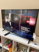 Front view of LG television powered on showing news broadcast with remote control placed beside it.