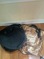 Two bags on the floor, one black backpack and one gold sequin tote