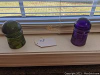 Two glass insulators on a windowsill, one dark green and one dark amethyst