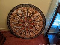 Round mosaic tile tabletop with geometric and floral design placed standing against a wall.