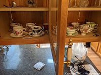 Photo showing multiple porcelain cup and saucer sets with a variety of floral designs displayed on a wooden shelf.