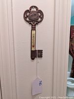Full view of the ornate visitor key-shaped wall thermometer hanging on the wall showing the full length with the temperature scale.