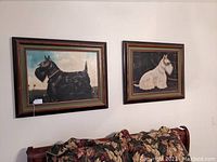 Pair of framed dog prints hanging on the wall above a couch with floral pillows.
