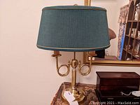 Full view of brass double arm lamp with blue pleated shade on a table, showing overall shape, size and condition.