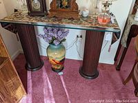 Full view of console table with fluted wood columns and glass top, shown with decorative items on top and vase with flowers below.