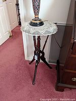 Fern stand showing full view with lace doily and lamp on top to show scale and use.