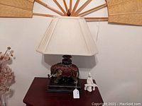 Front view of lamp showing carved elephant base and cream pleated lamp shade on red-brown table