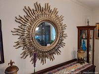 Front view of large round sunburst mirror mounted on wall with visible room reflection.