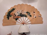 Full view of large bamboo wall fan hanging on wall above lamp.