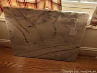 Front view of large rectangular marble charcuterie board showing white marble with gray veining and price tag.