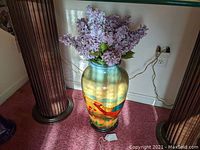 Full view of tall pottery vase with artificial lilac flowers inside. Vase is hand-painted with colorful pheasant design.