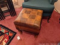 Footstool from angled front view showing top patchwork leather and wooden legs.