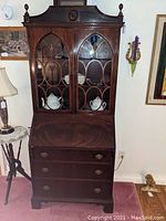Front view of the mahogany Federal-style secretary desk with glass front bookcase top, showing decorative finials and rosette pediment.