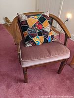 Front view of walnut wraparound arm chair with dusty rose velvet seat and crazy quilt throw pillow