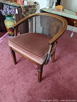 Full front view of mid-century walnut chair with cane back and dusty pink upholstered seat, set on pink carpet with surrounding furniture.