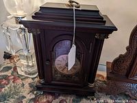Front view of dark wooden bracket clock with glass door, Roman numeral dial, and decorative gold-tone accents.