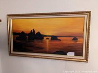 Full view of the ocean sunset painting with gold frame hung on wall.