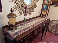 Pair of matching boudoir lamps on top of a wooden console table with decorative runner and mirror behind.