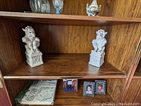 Pair of white porcelain foo dog statues displayed on wooden shelf, front angle