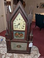 Full front view of wooden double steeple clock showing case, spires, dial, and both reverse painted glass tablets