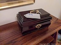 Closed view of the small mahogany stained jewelry box showing wood finish and gold-tone hardware.