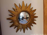 Full front view of small sun-shaped convex mirror with gold frame hanging on wall.