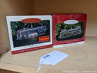 Two boxed Hallmark Keepsake Lionel train ornaments side by side on shelf