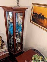 Full view of trapezoidal shaped wooden display cabinet with glass panels showing multiple figurines inside.