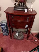 Front view of the two drawer bow front stand, showing drawer pulls, lock on top drawer, and top surface with decorative items.