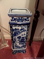 Tall square blue and white Chinese floor vase showing front scenic design with pagodas, water and trees.