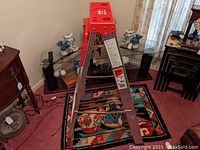 Full view of the Werner aluminum step ladder standing on a colorful rug indoors showing its fold-out design and red top cap.
